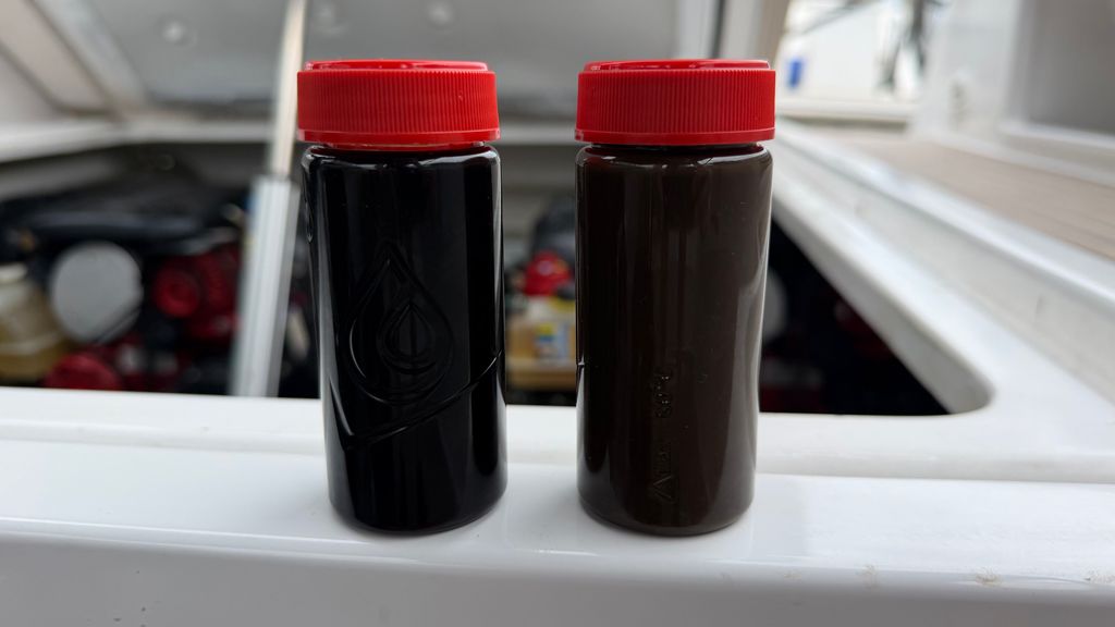 Two oil sample vials with red caps standing on a gunwale beside an open engine hatch, drawn during an engine survey