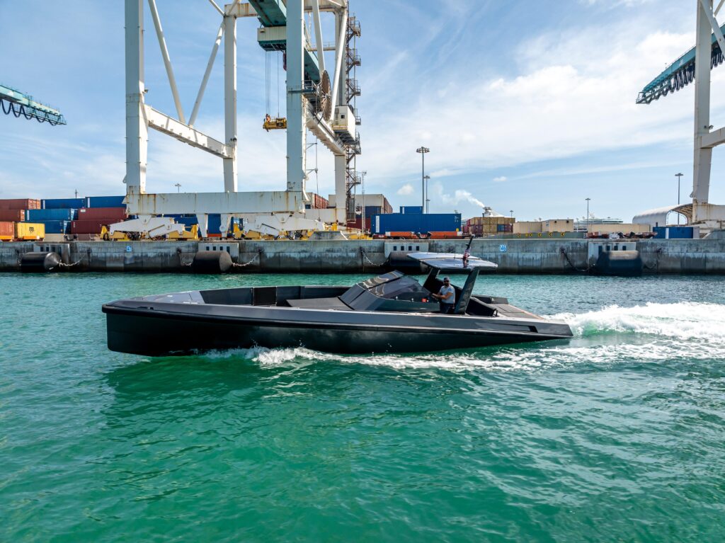 A dayboat running past container cranes at the port, where an imported hull clears customs